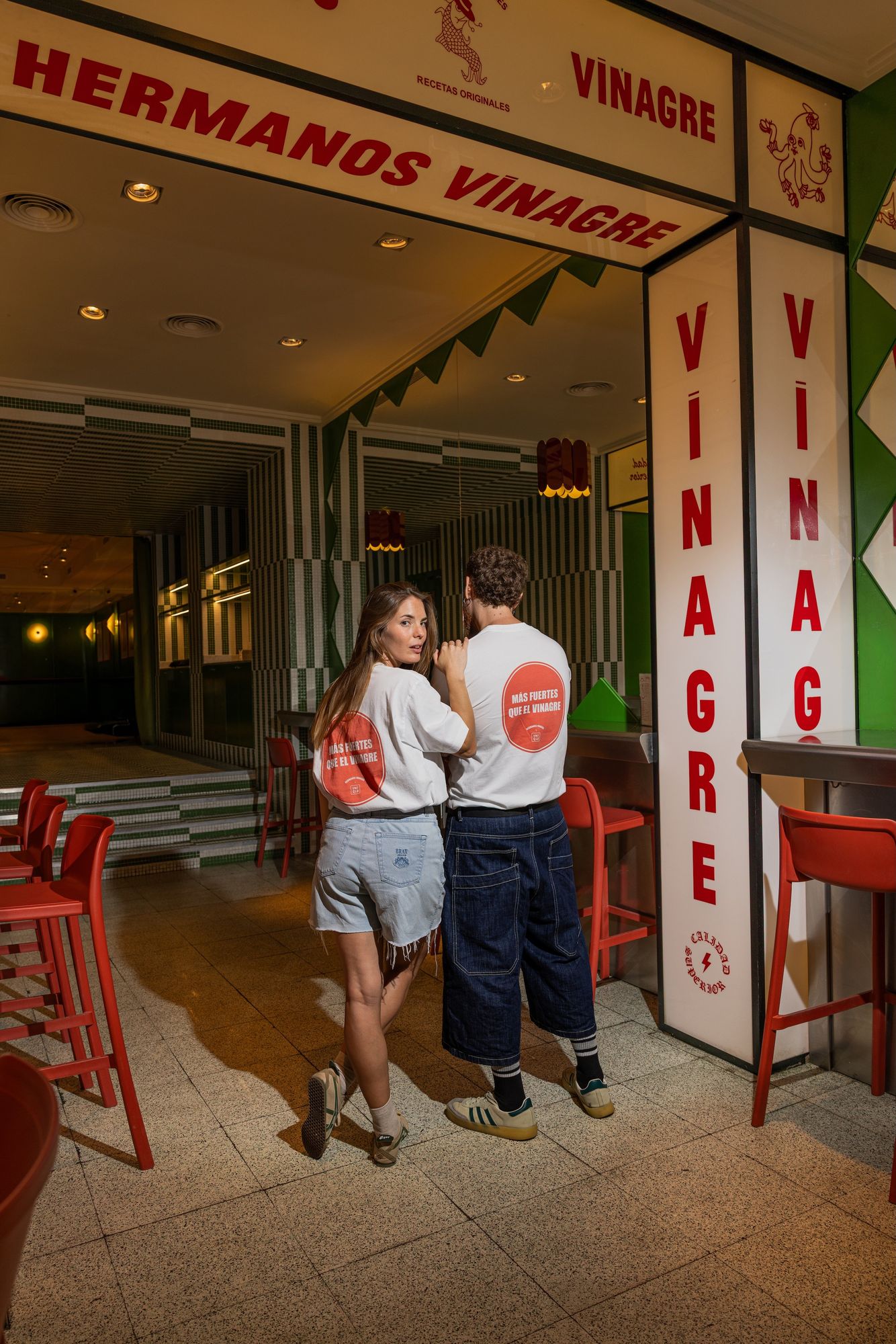 A couple wearing Hermanos Vinagre × UNIQLO T-shirts at the entrance of a bar